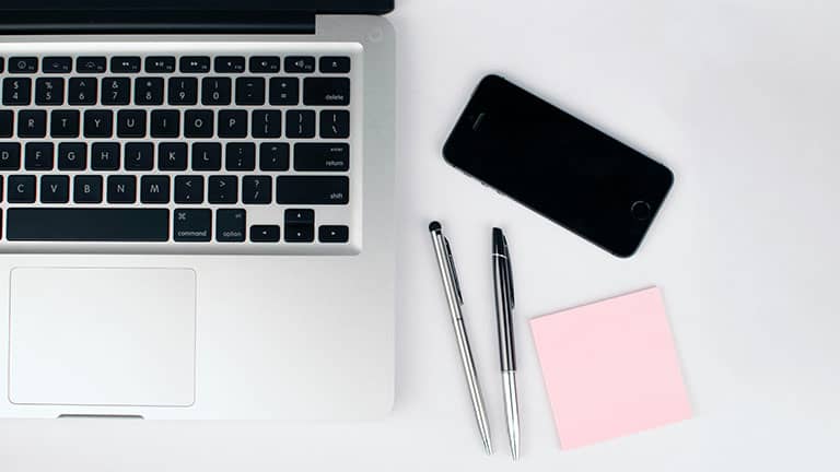 Two pens beside macbook along with pens, notebook and iphone