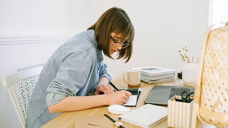 Woman writing on a notebook on a wooden table with coffee