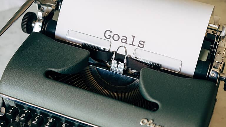 Green old typewriter on brown wooden table with text goals